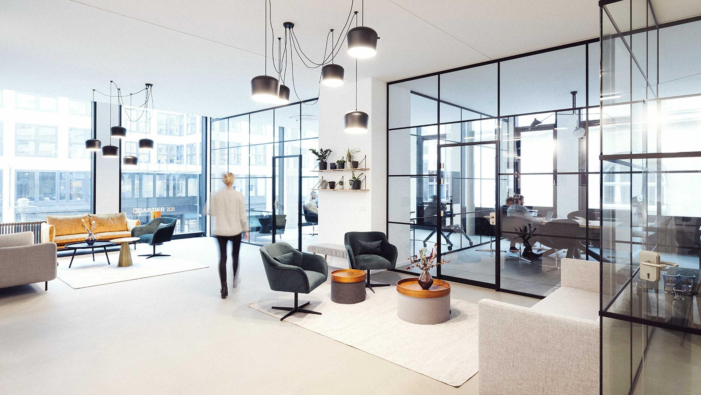 Modern office interior with glass walls, pendant lighting, and stylish furniture.