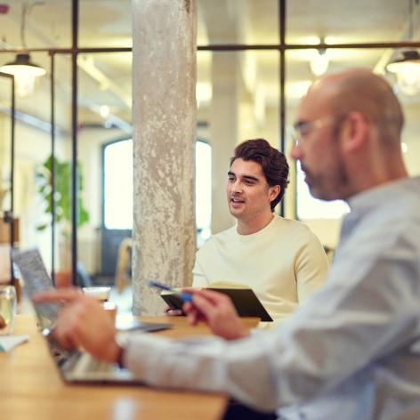 Two professionals working at a table with laptops in a modern office setting.
