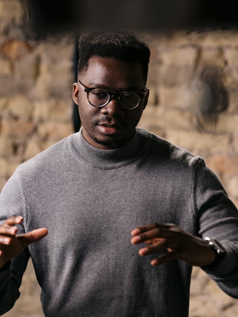 Homem de suéter cinzento e óculos a gesticular com as mãos