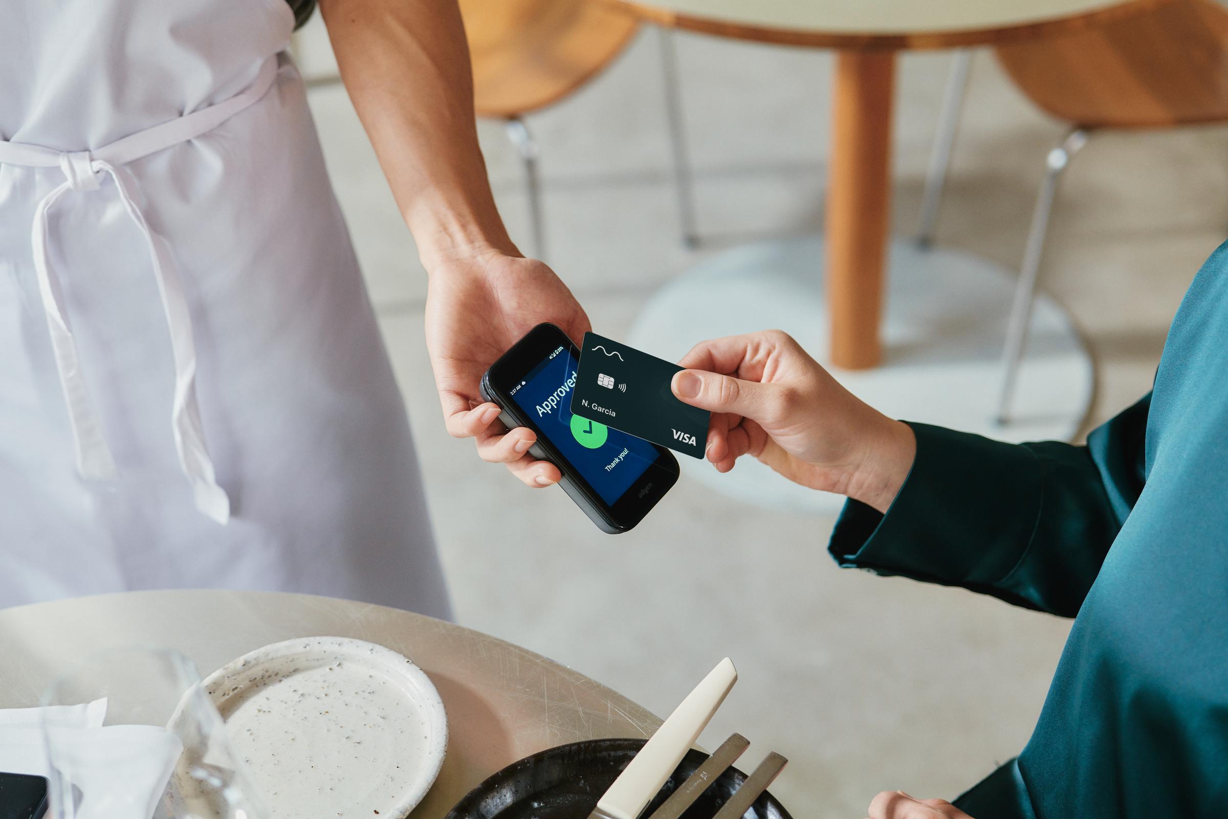 A woman in restaurant paying for food by tapping a VISA card on Adyen's AMS1 terminal.