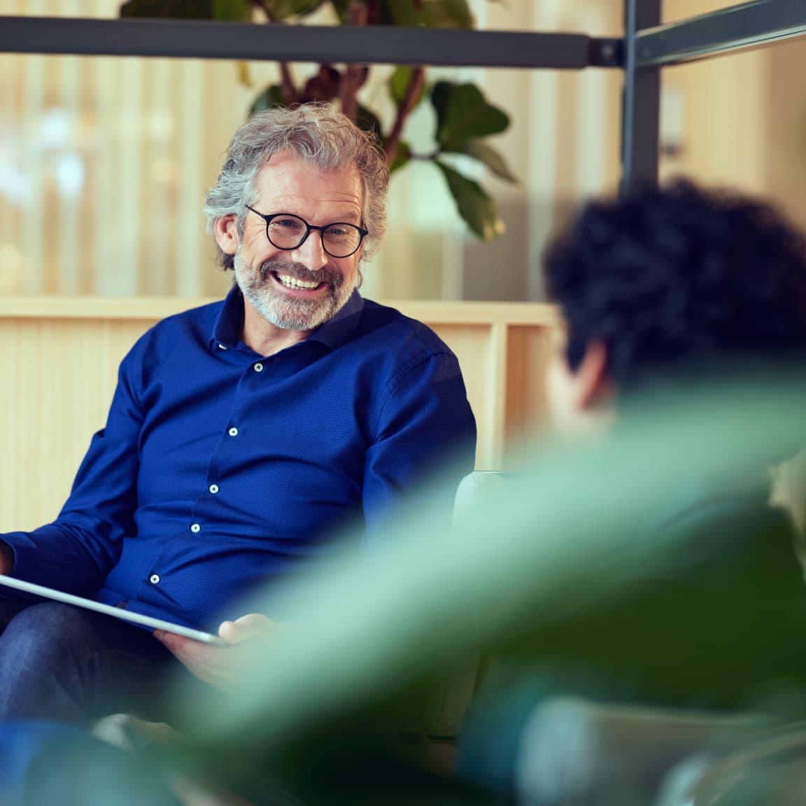 Leende skäggig man i blå skjorta i samtal med en annan person.