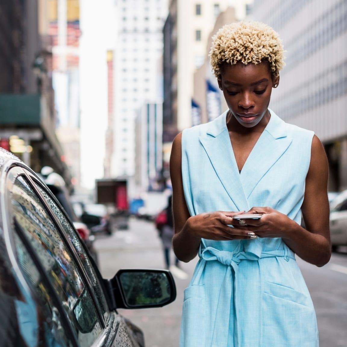 Une femme en robe bleue utilisant un smartphone dans une rue de la ville.