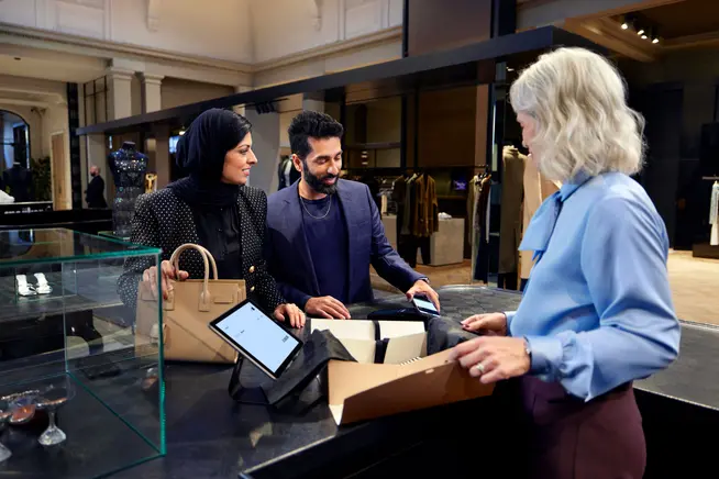 Una coppia in un negozio di moda di lusso che paga per il loro acquisto toccando il loro iPhone sul terminale S1F2 di Adyen.