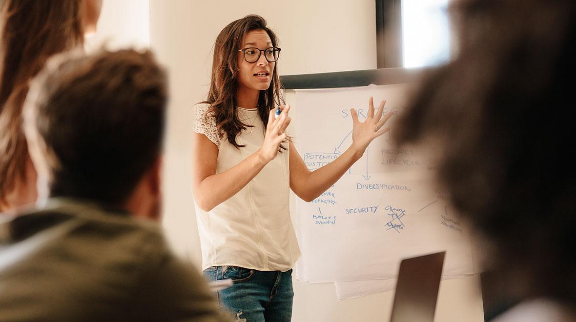 Mulher apresentando um plano estratégico em uma lousa branca para colegas em uma reunião.