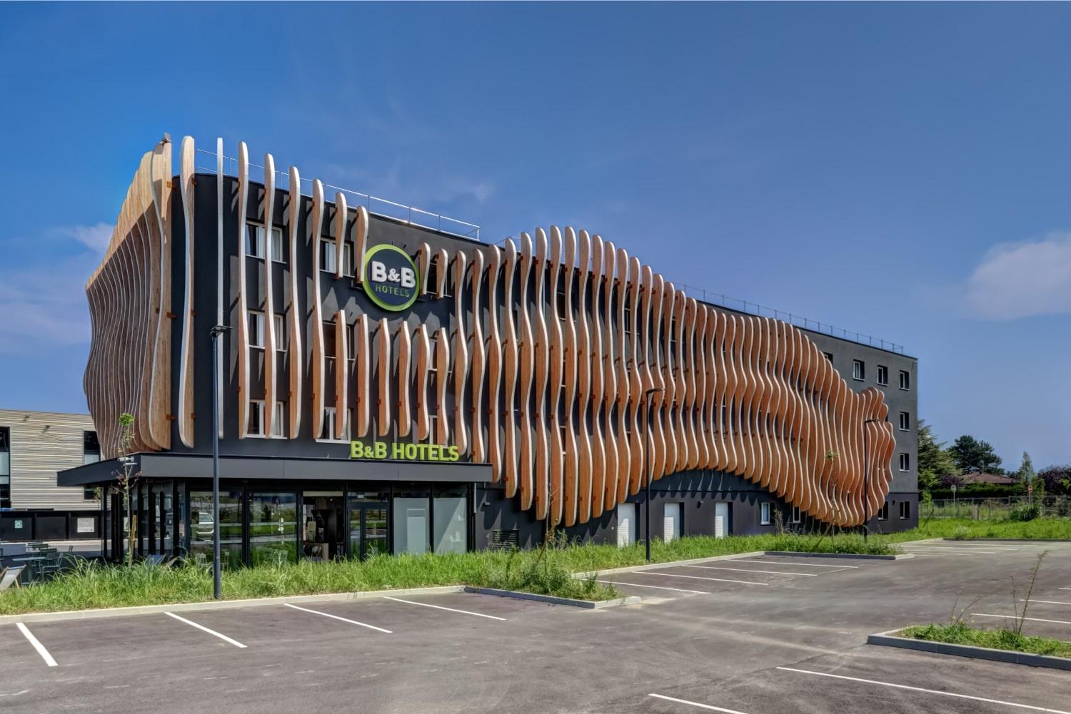 Modern hotel building with unique wavy wooden facade design under a clear blue sky.