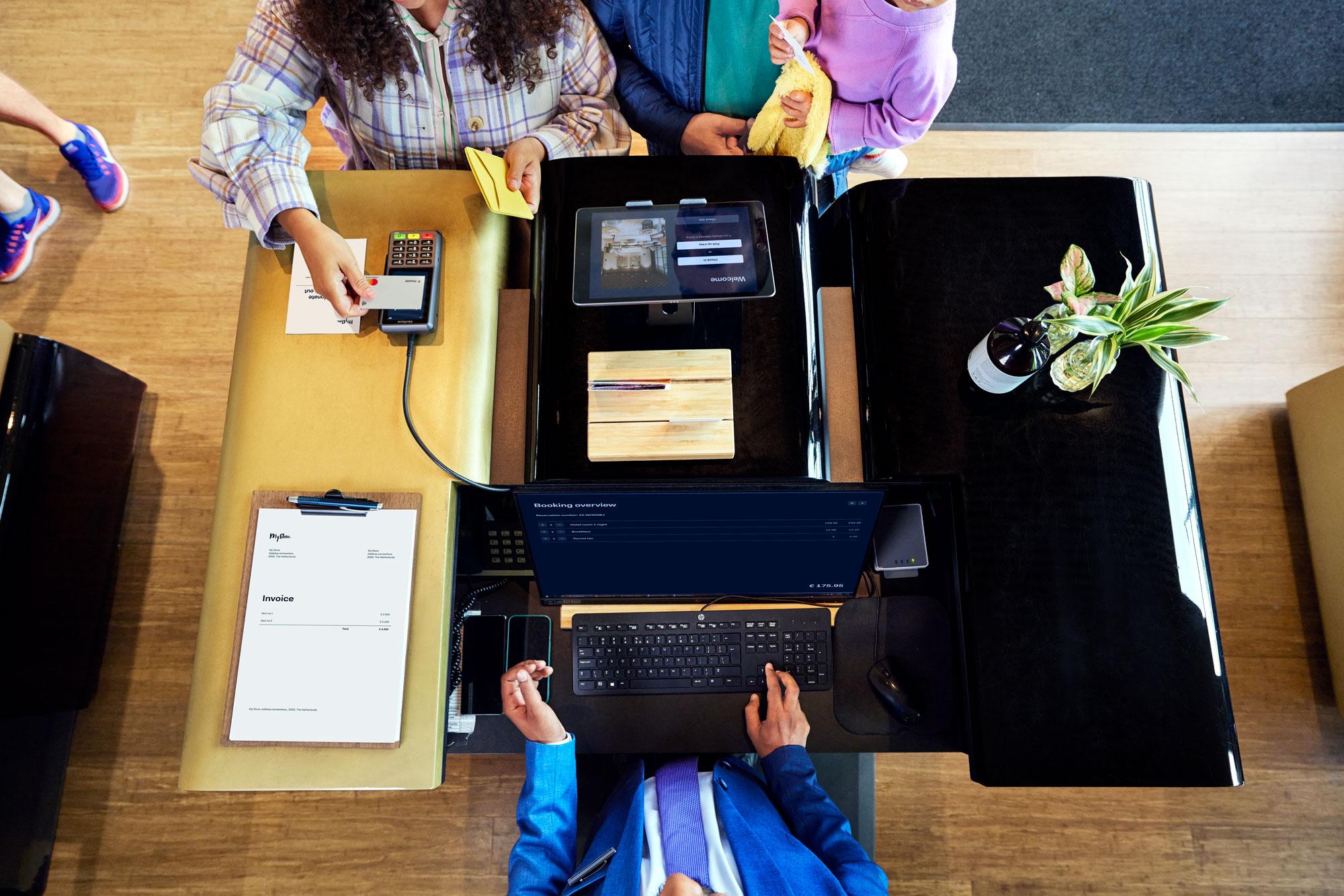 A family at a hotel reception desk making a payment by tapping a card on Adyen's P400 Plus terminal.