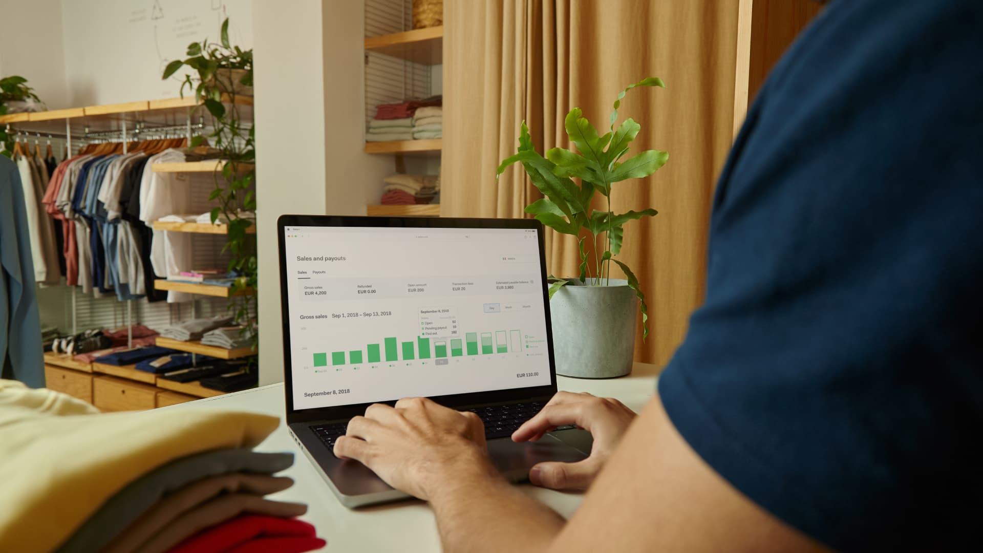 Person analyzing Adyen sales and payouts data on laptop in a clothing shop.
