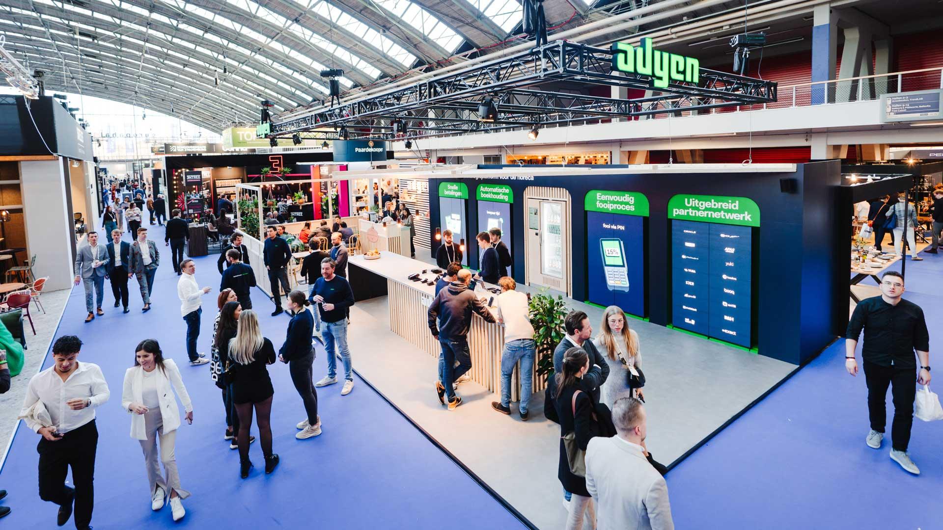 Drukke beurshal met mensen rond Adyen-standen die betalingsoplossingen bespreken