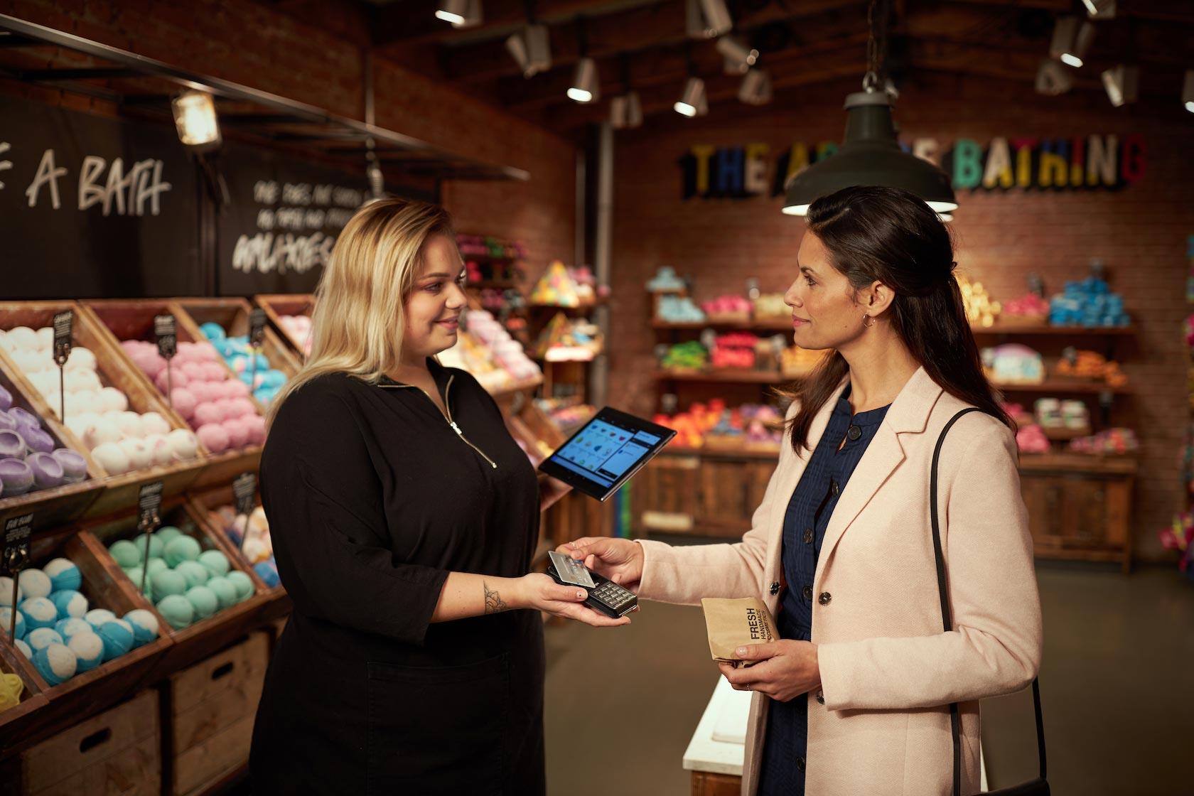 Händler, der ein digitales Tablet verwendet, um einem Kunden beim Bezahlen mit Karte in einem farbenfrohen Geschäft zu helfen
