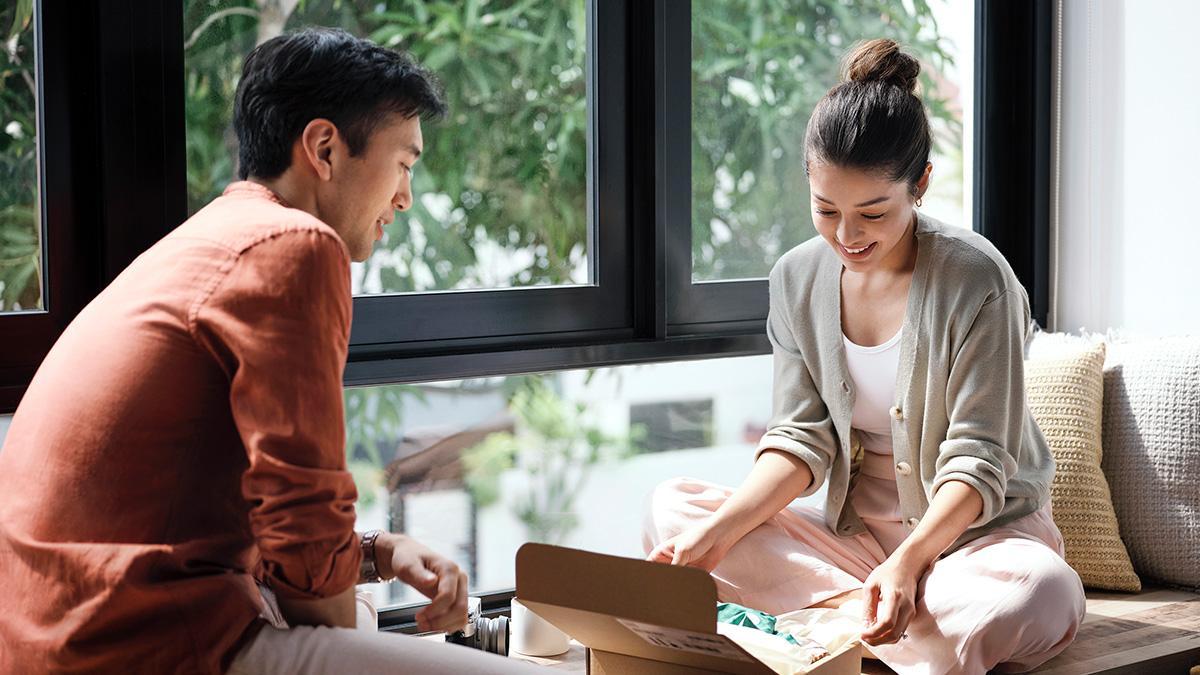 Two individuals sitting by a window looking at items inside an open box.