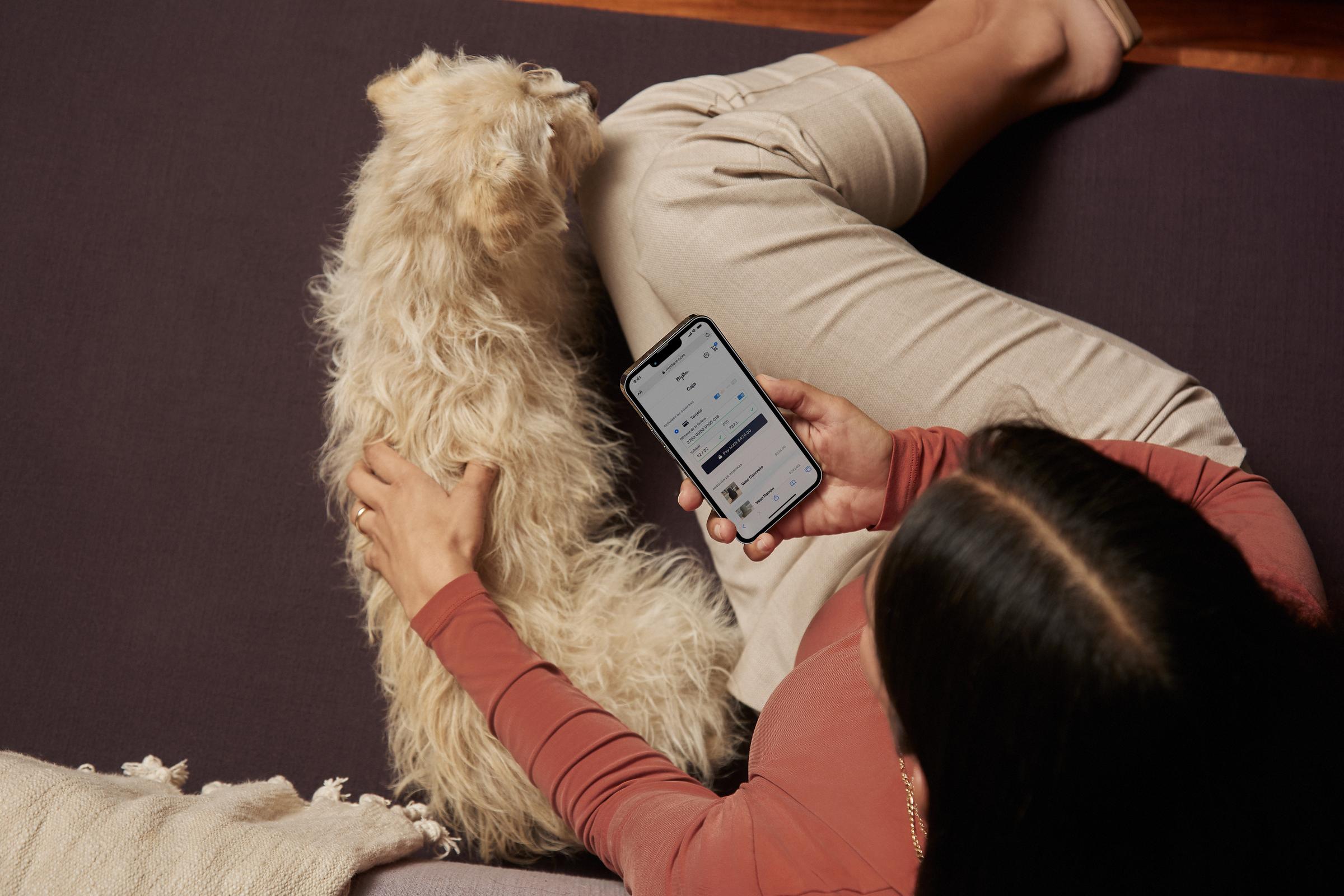 Persona relajada con un perro mientras sostiene un smartphone que muestra la interfaz de la aplicación Adyen.