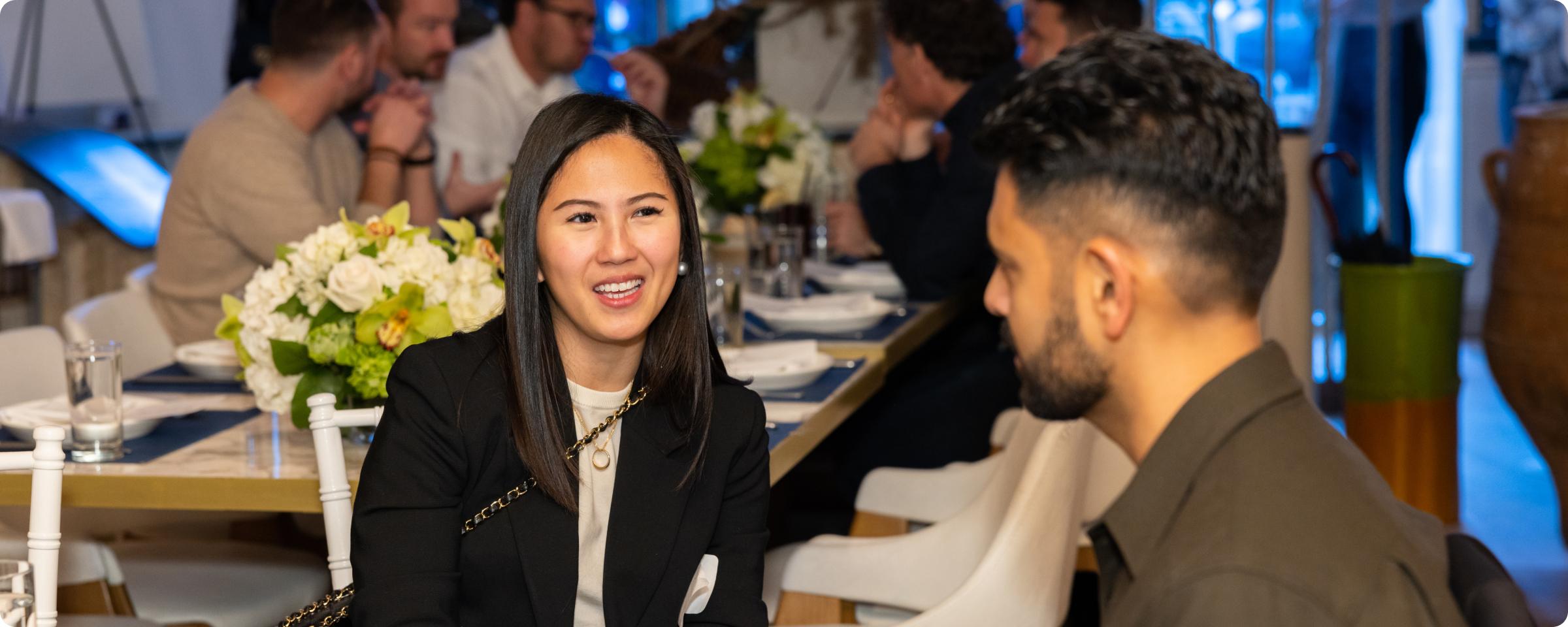 Woman and man engaging in conversation at a dining table with others in the background.