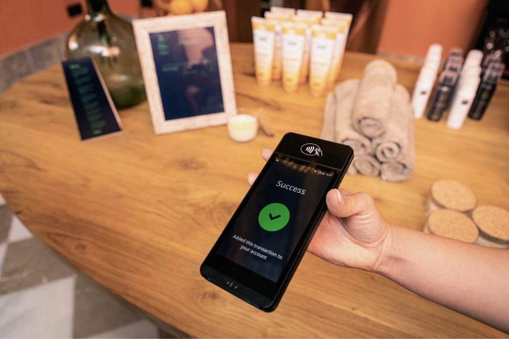 Primer plano de una mano sosteniendo un smartphone que muestra una pantalla de transacción exitosa en la aplicación Adyen.