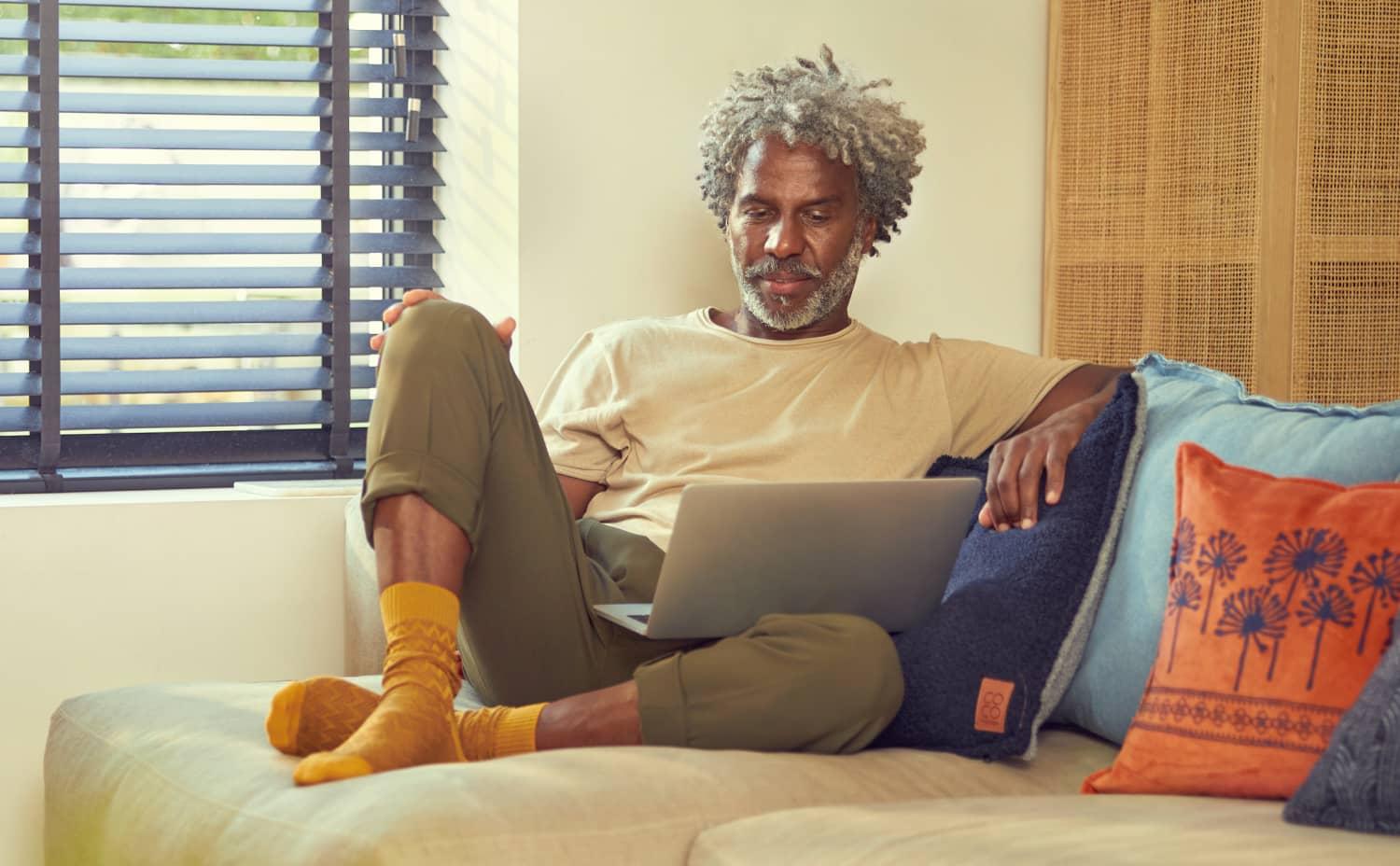 Mand sidder komfortabelt på en sofa og bruger en bærbar computer.