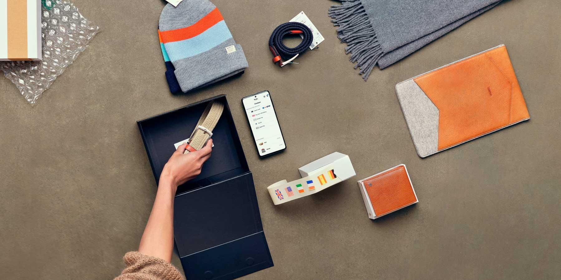 Vista dall'alto di una persona che imballa un pacco con merce e utilizza l'app di pagamento Adyen su uno smartphone.