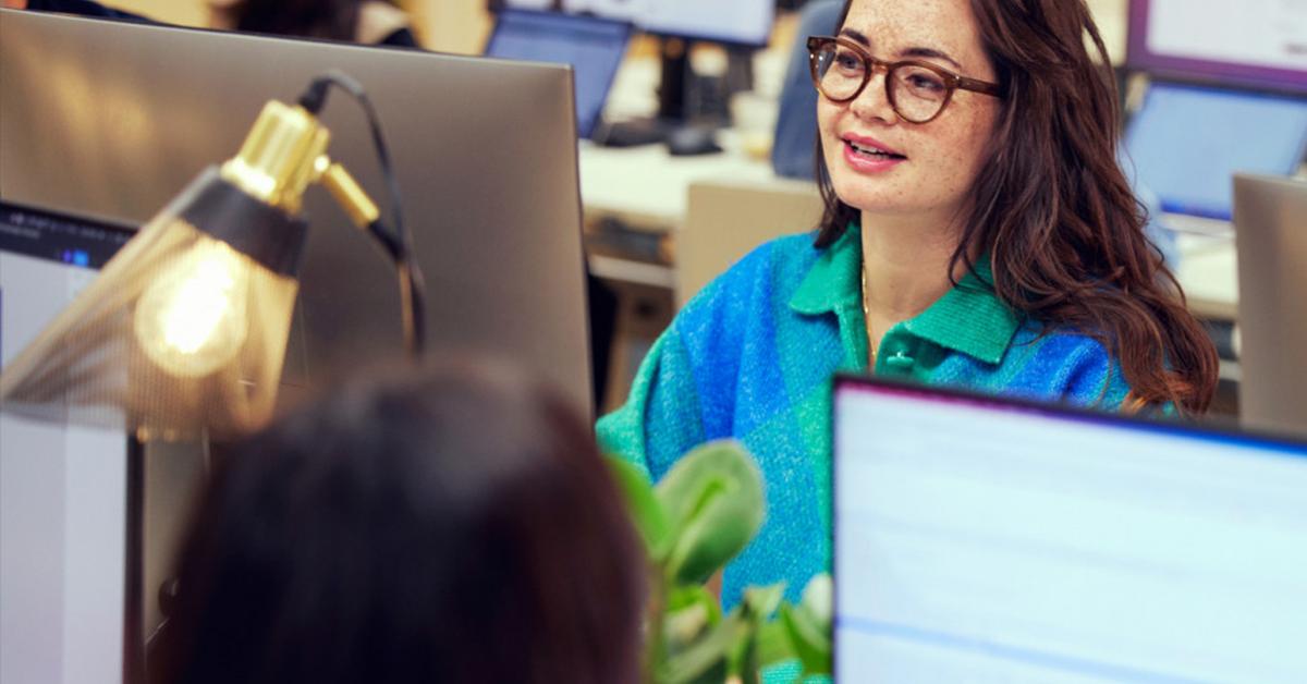 Smiling woman with glasses working at a computer in an office environment.