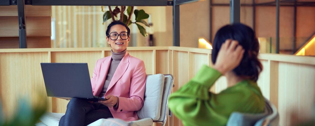 Two professionals in a casual meeting with one holding a laptop.