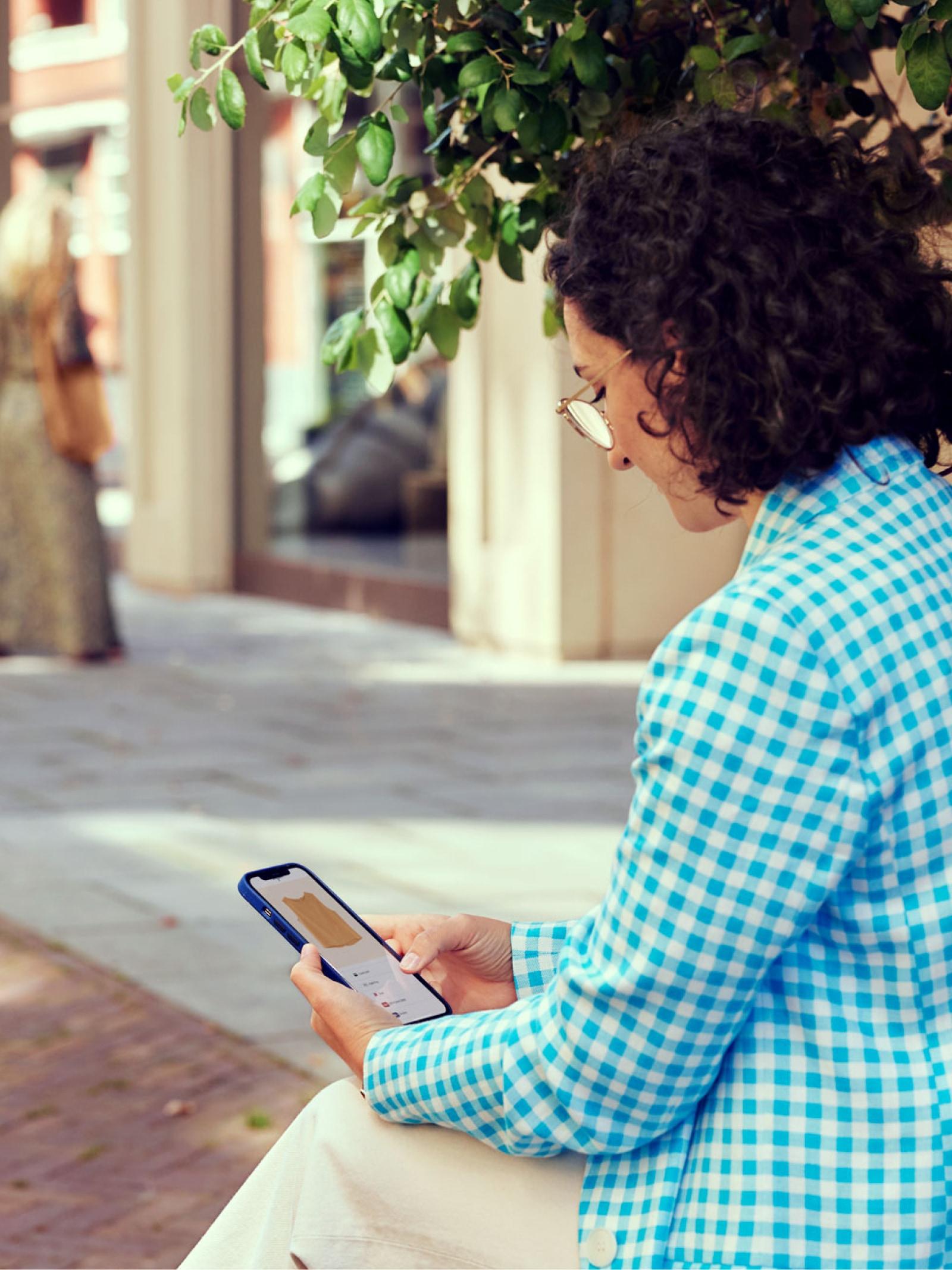 Persona seduta all'aperto che utilizza uno smartphone per accedere a un servizio, possibilmente coinvolgente un prodotto Adyen