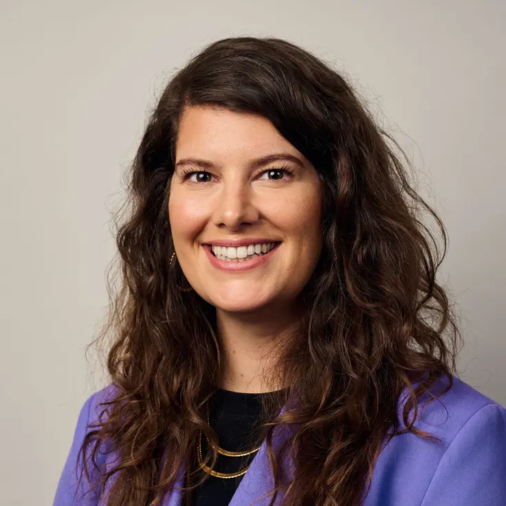 En leende kvinna med lockigt hår som bär en blå kavaj och en guldhalsband.