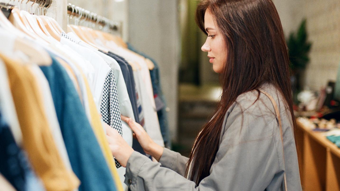 Frau durchstöbert Kleidung an Verkaufsständern.