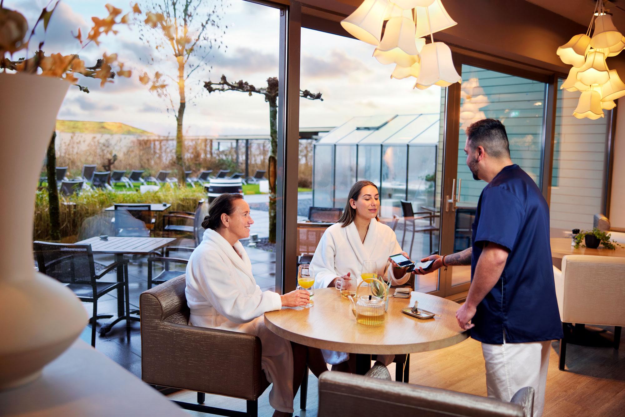 Two women at a table paying for spa and wellness by tapping their smartphone at Adyen's S1E terminal.