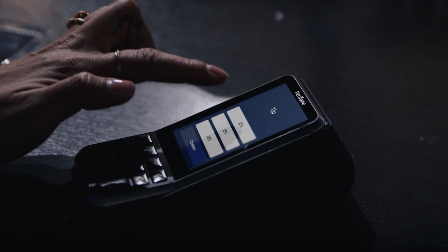 Primo piano di una mano che seleziona un importo di mancia su un terminale di pagamento Adyen