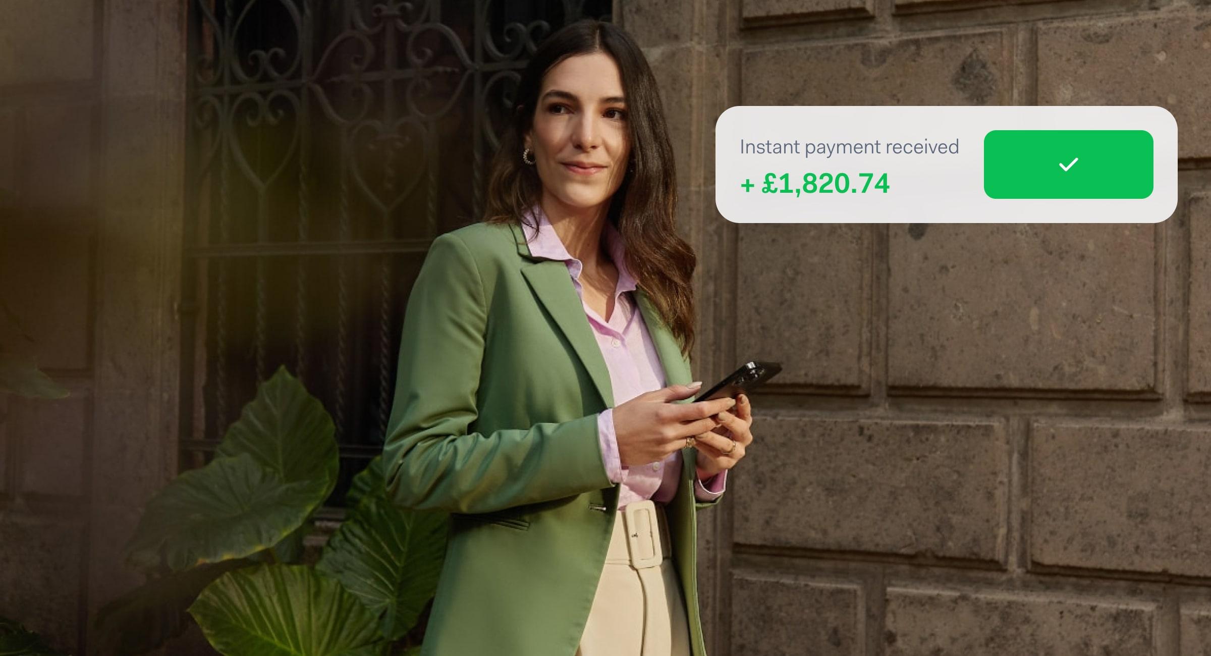 Woman in a green blazer receiving an instant payment notification for £1,820.74 on her phone.