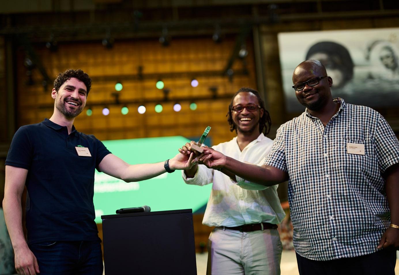 Trzech uśmiechniętych mężczyzn podających sobie rękę, trzymających nagrodę.