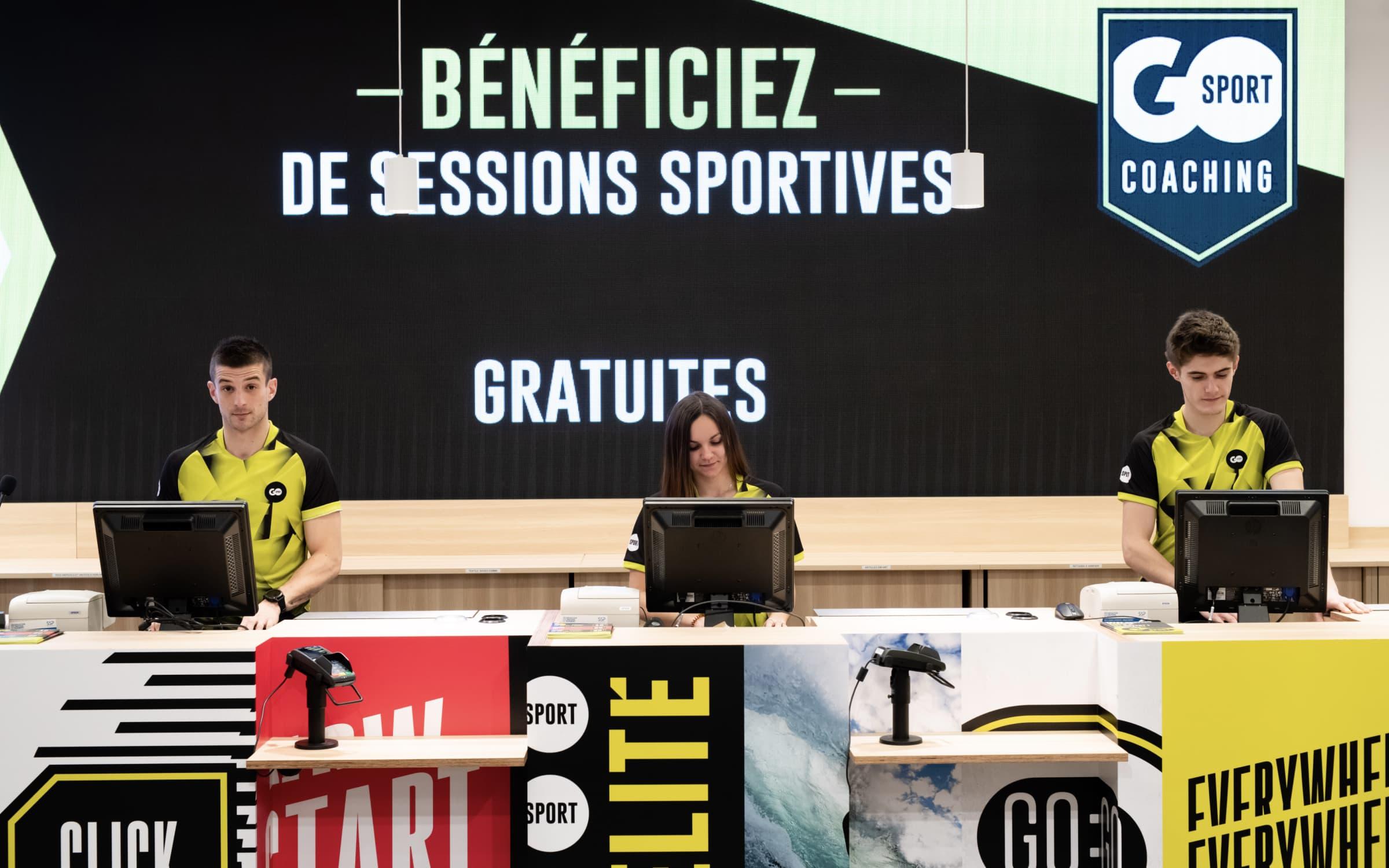 Personnel au comptoir d'information d'un magasin de sports avec des panneaux promotionnels en arrière-plan.