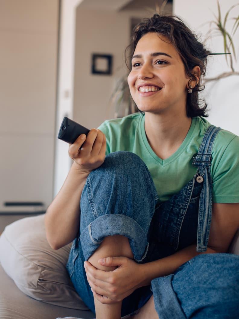 Smiling person sitting with legs crossed holding a remote control.