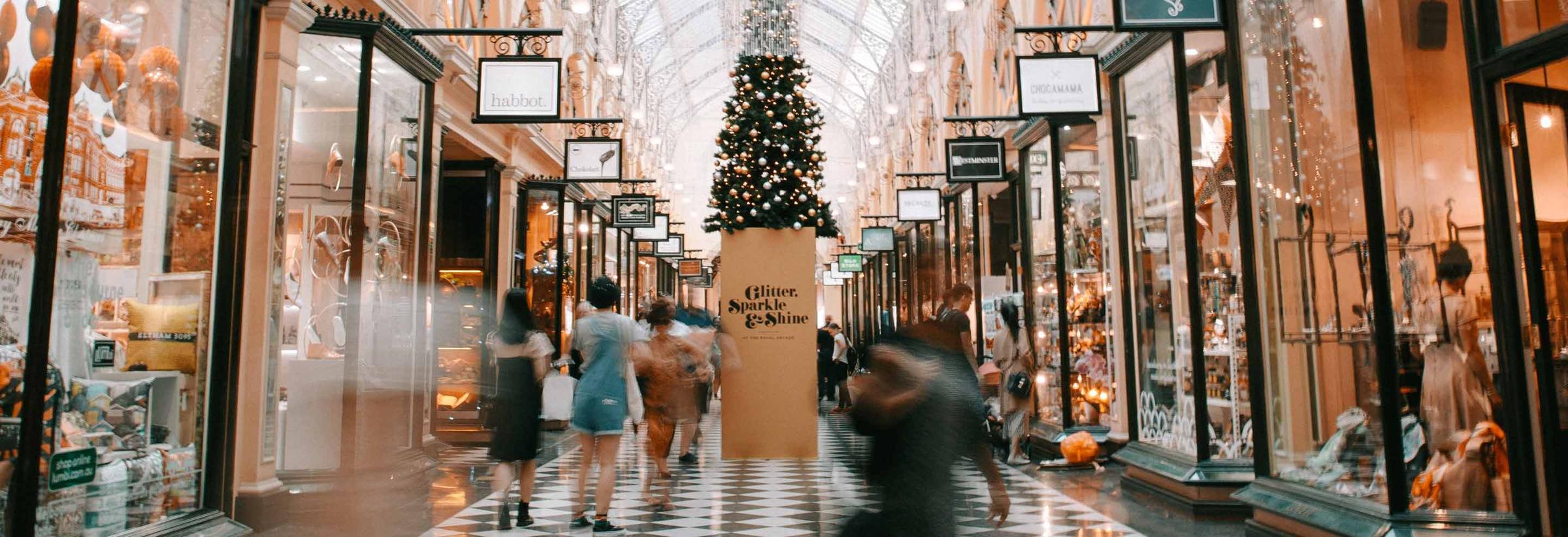 Compradores caminando dentro de un bullicioso centro comercial interior decorado con un árbol de Navidad y luces festivas.