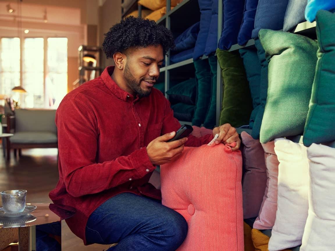 Man sitting in a home decor store, comparing fabric swatches on his phone.