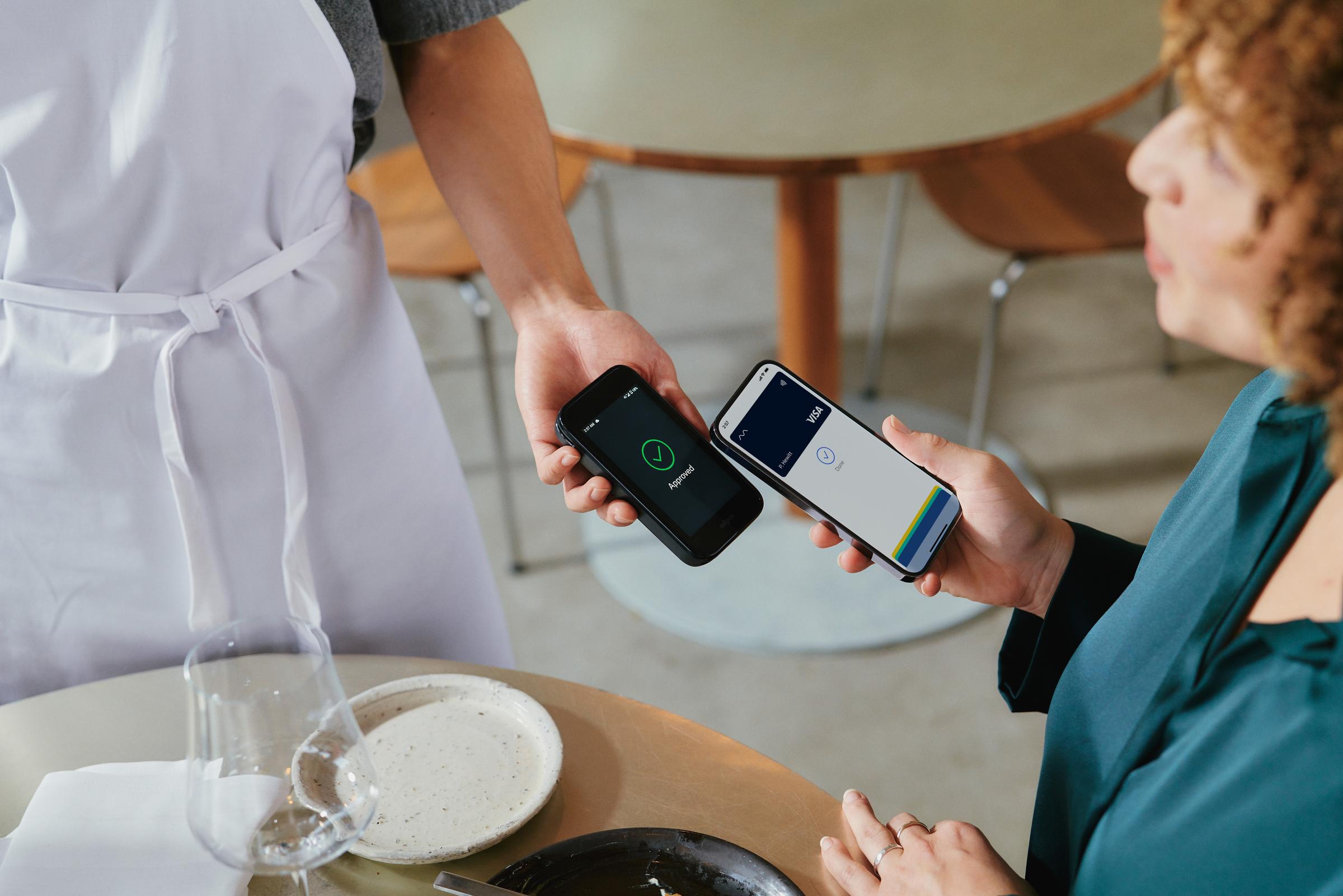 A woman in restaurant paying for food by tapping a smartphone on Adyen's AMS1 terminal.
