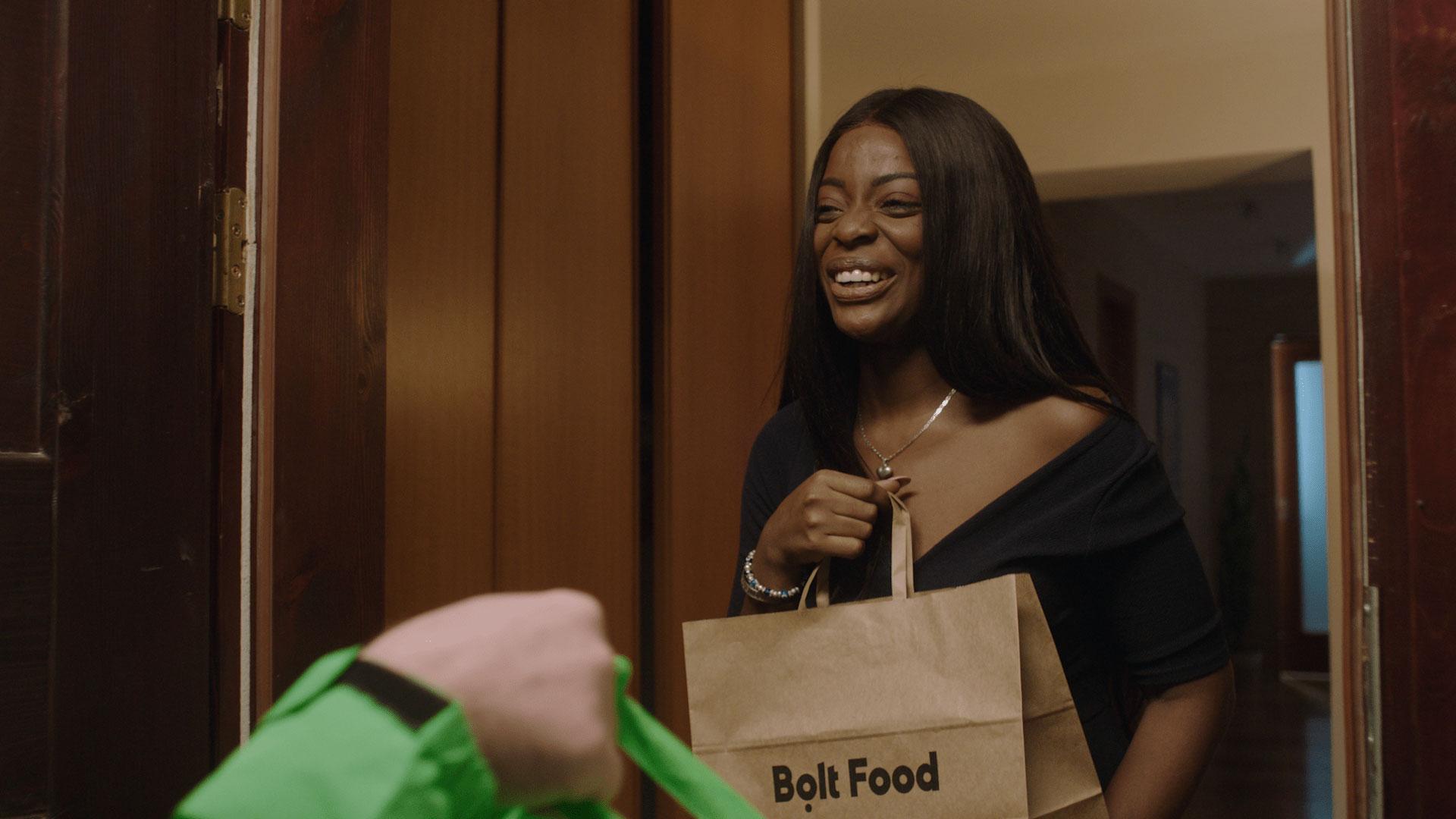 Happy woman receiving a Bolt Food delivery bag from a delivery person at her door.