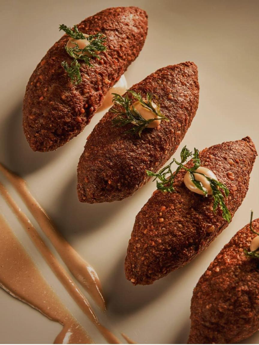 Primer plano de kibbeh, un plato de carne del Medio Oriente, decorado con hierbas y salsa.