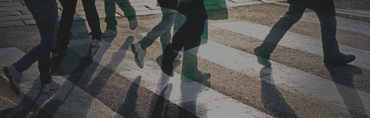 Several people walking across a pedestrian crosswalk casting shadows on the ground.