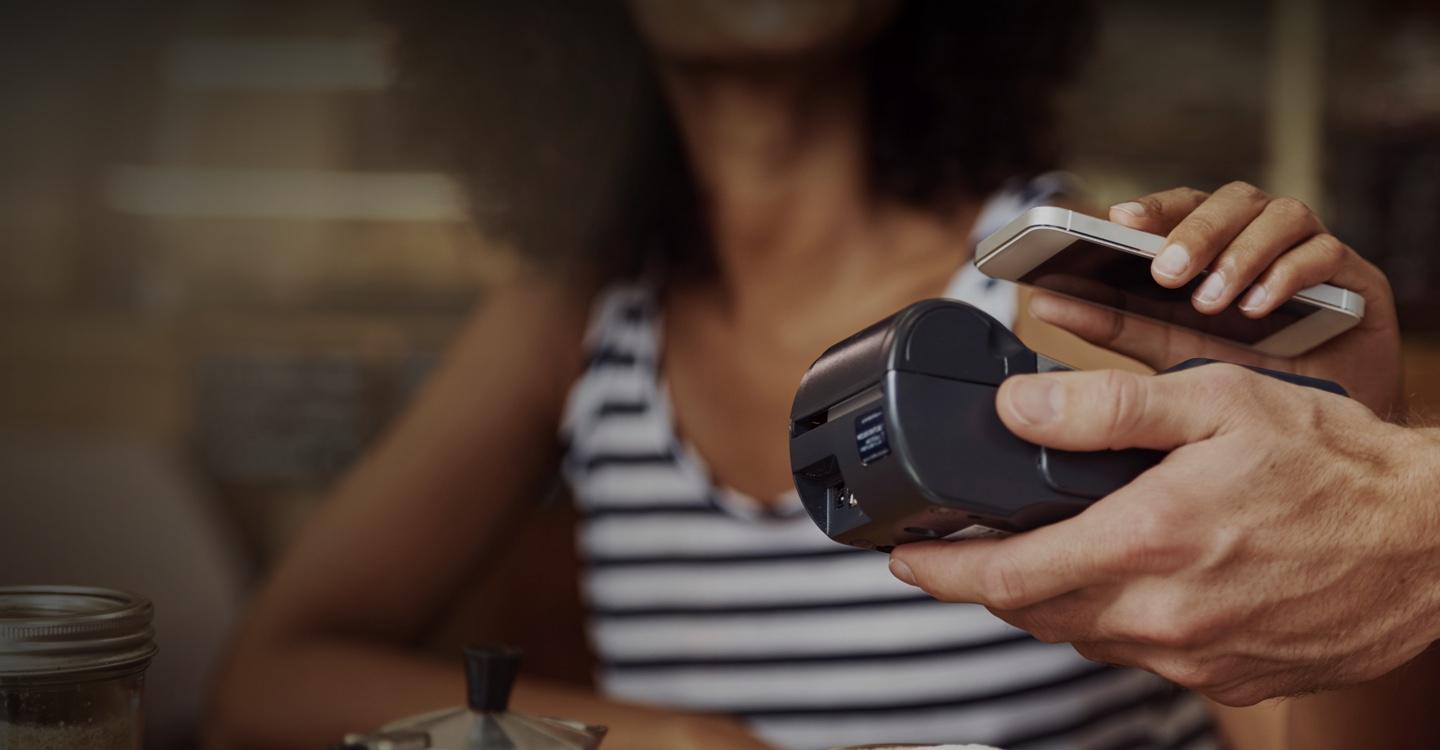 Persona che utilizza uno smartphone per effettuare un pagamento senza contatto con un lettore di carte Adyen