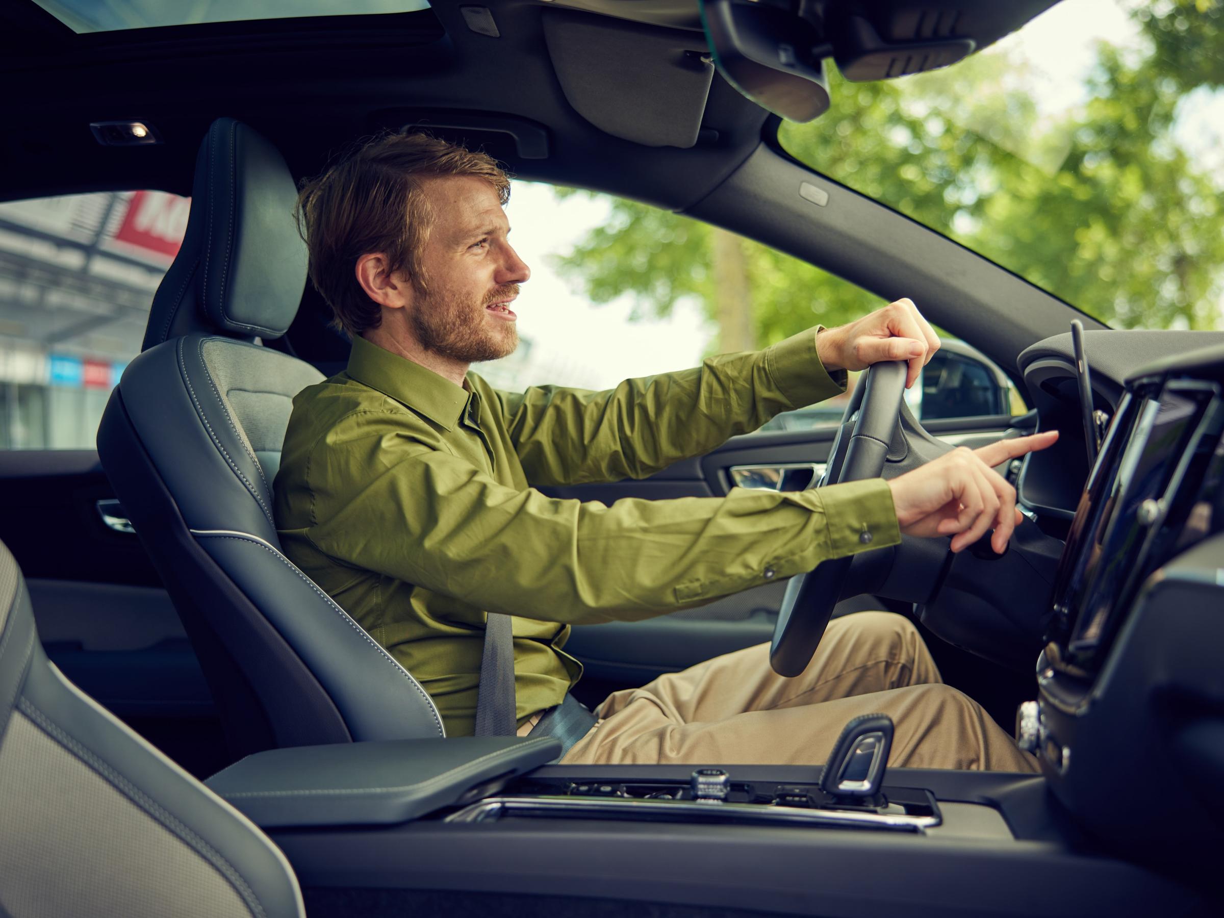 Man in a green shirt driving and interacting with a car's touchscreen interface.