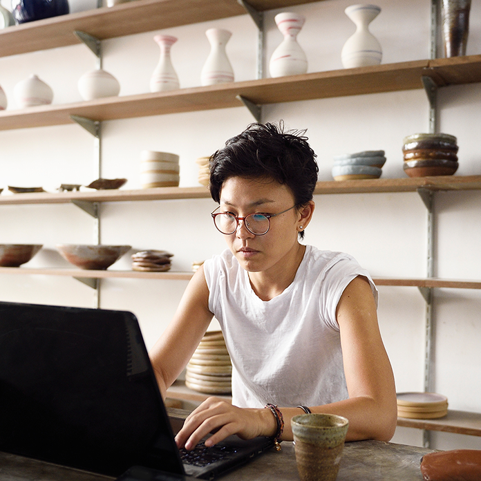 A business owner in her pottery store, sitting behind a laptop.