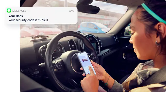 Person sitting in the driver's seat of a car, checking a security code on a smartphone.