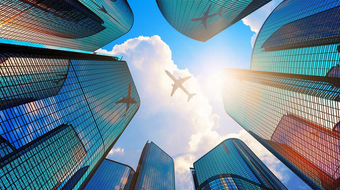 Avião voando sobre arranha-céus contra um céu ensolarado