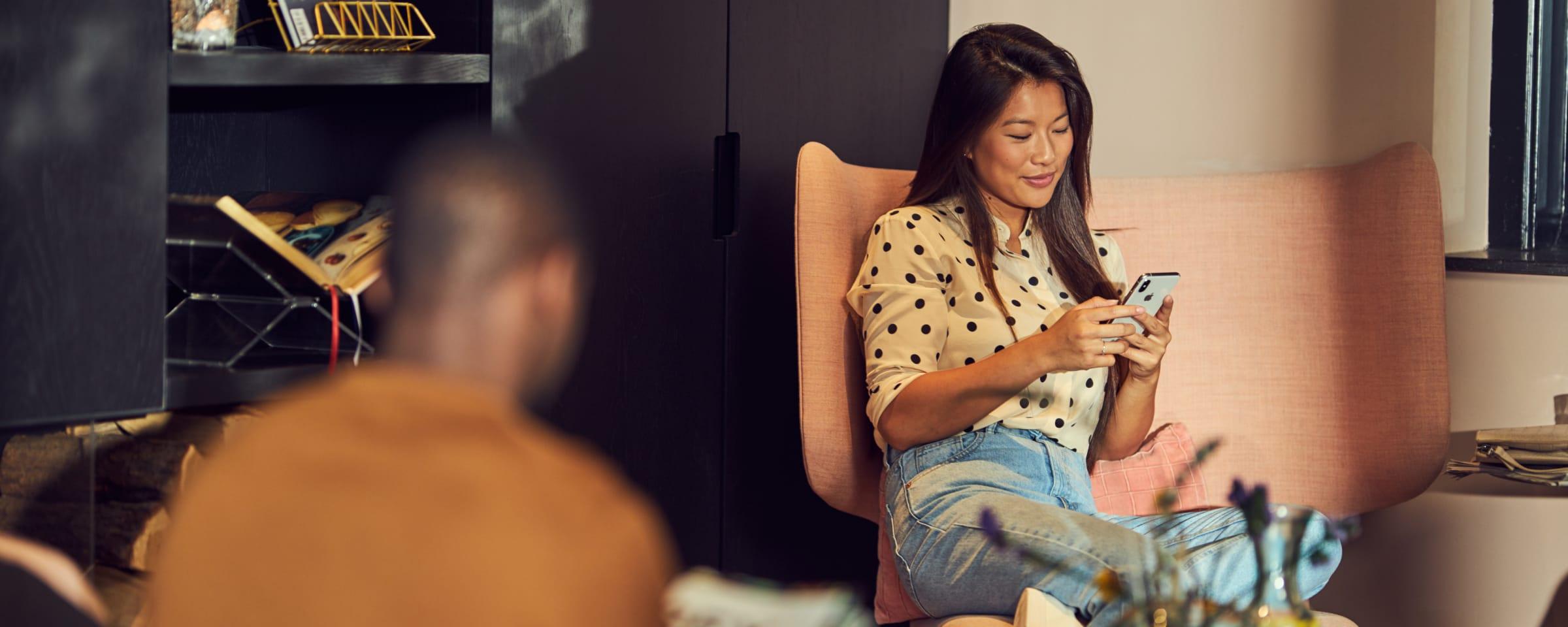 Woman sitting comfortably and using her smartphone in a cozy room setting with soft lighting.