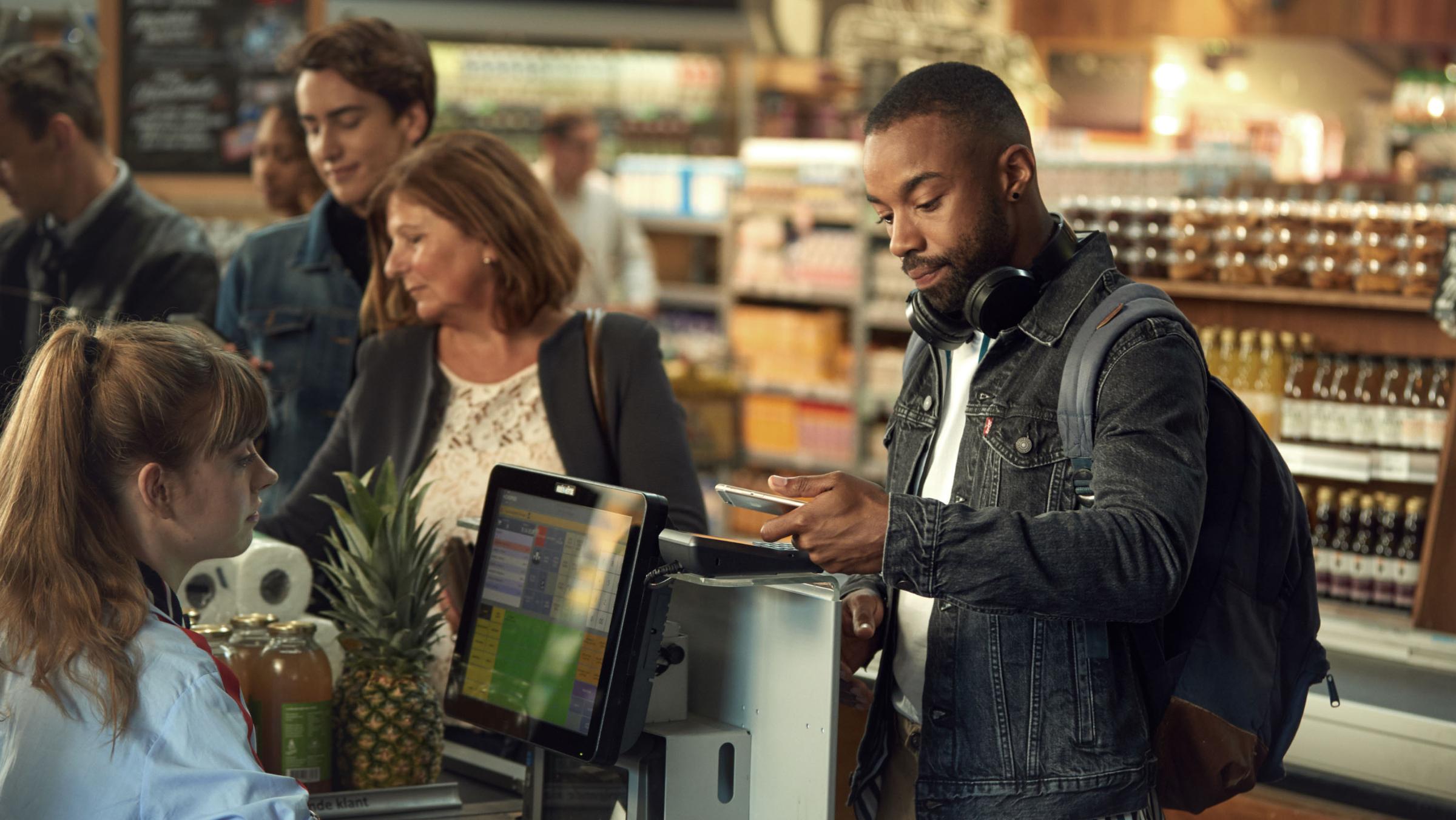 Man using smartphone to make a payment at a grocery store checkout.