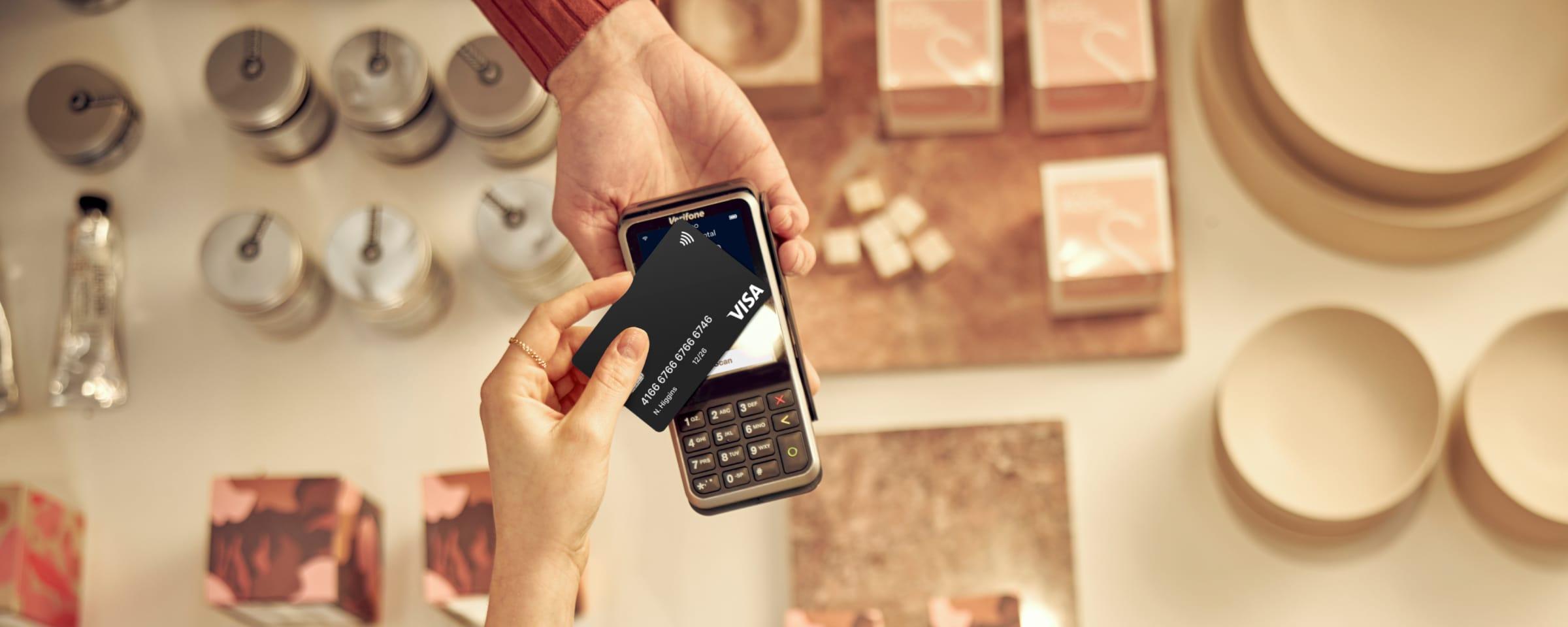 Person som gjør en kontaktløs betaling med et Visa-kort på en betalings-terminal over en butikkdisk.