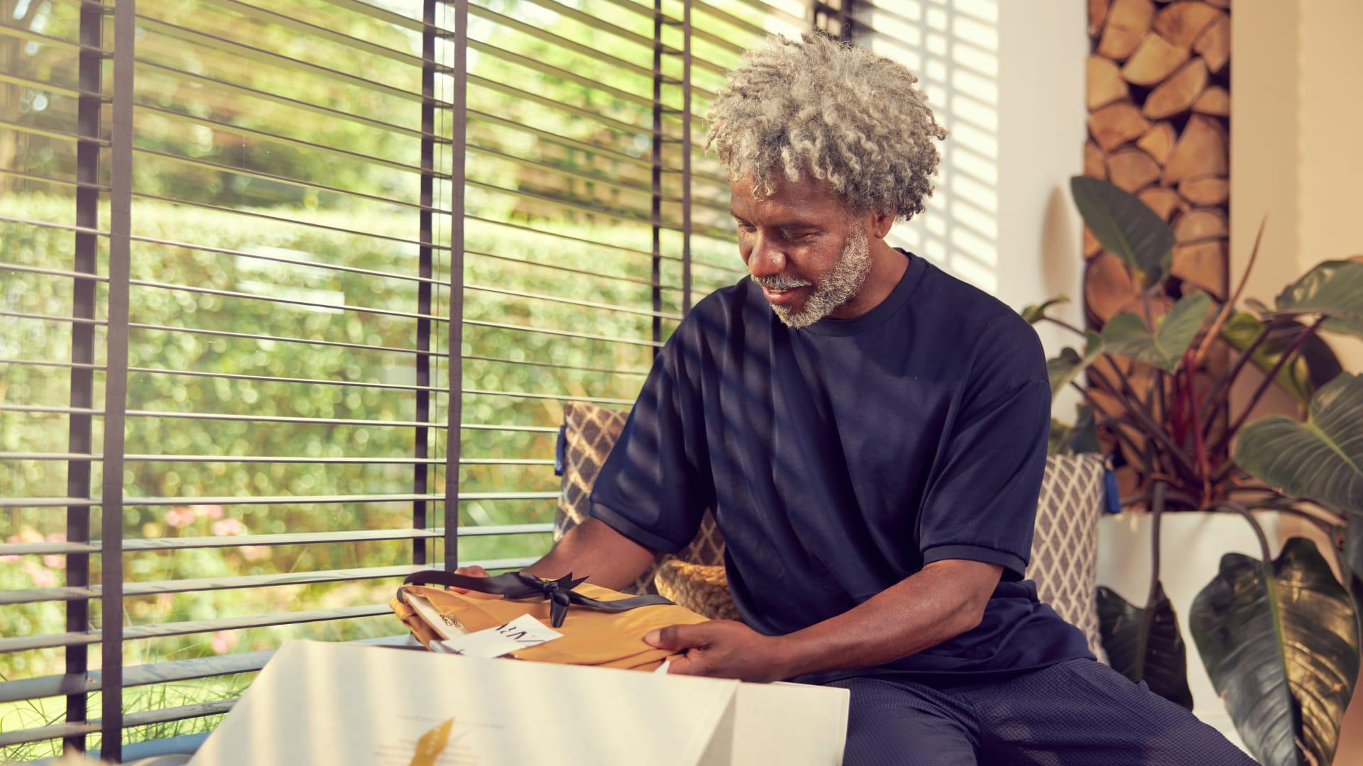 Man sitting by a window smiling and holding a packaged gift.
