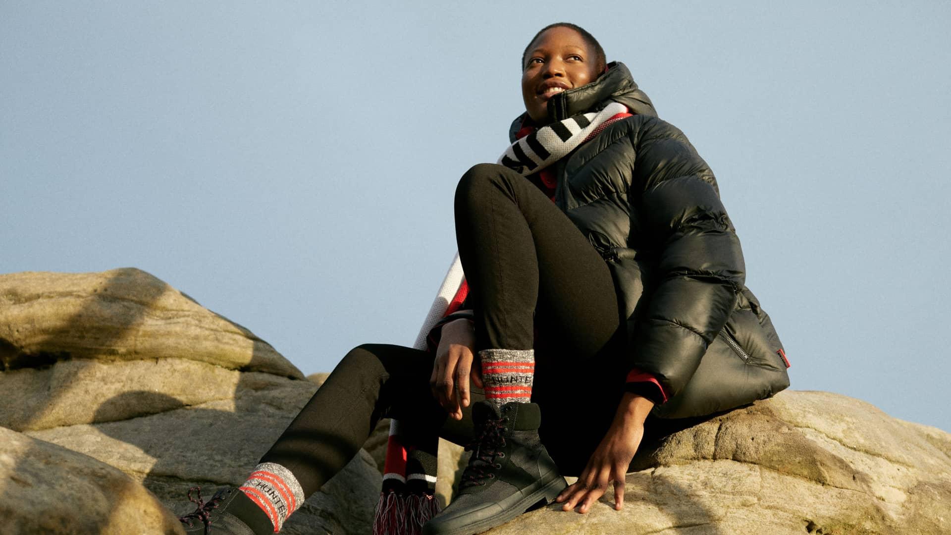 Person sitting on a rock outdoors wearing warm clothing and looking up at the sky.