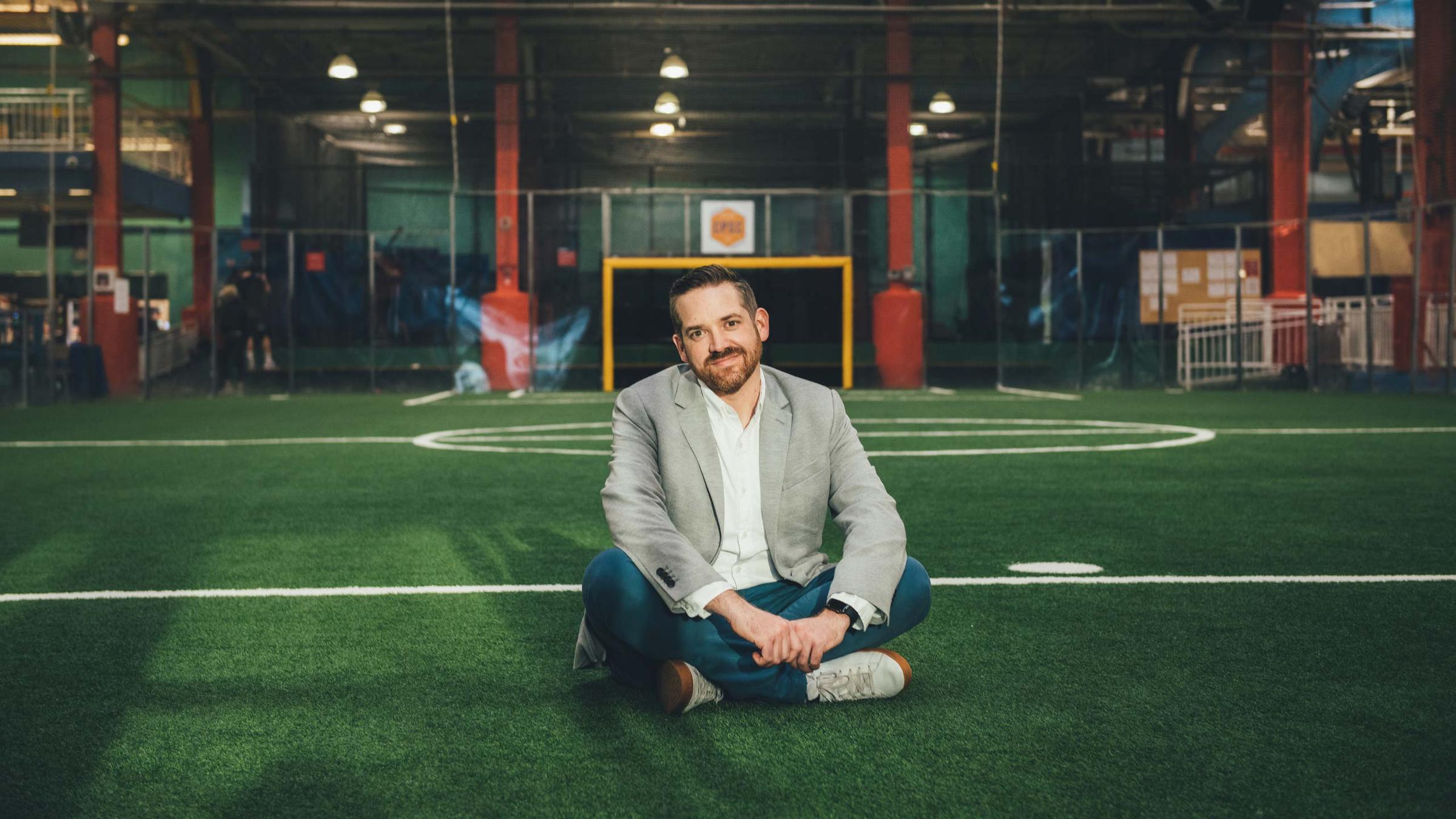 Man sitting on an indoor soccer field with a smile.