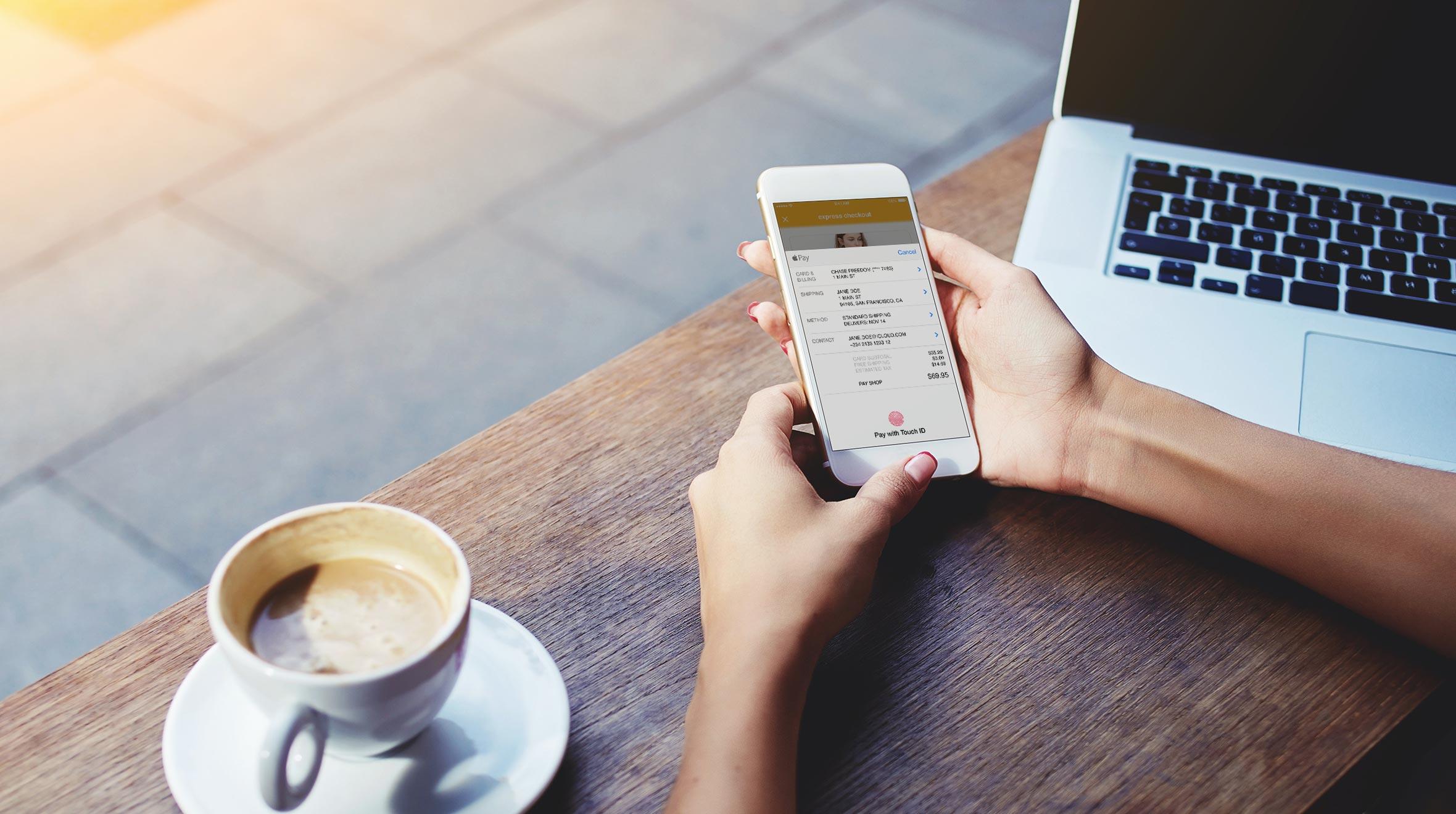Person, die ein Smartphone verwendet, um eine Zahlung über eine Mobile-App neben einem Laptop und Kaffee abzuschließen.