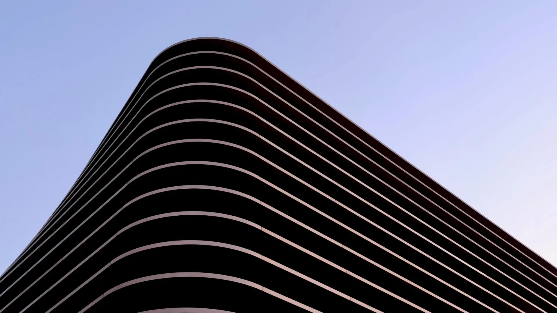 Curved modern building in Poland with layered balconies against a clear sky at twilight.