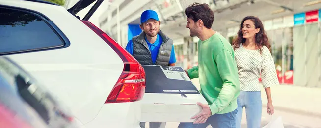 Delivery man handing over a large package to a smiling man with a woman beside him in a city setting.